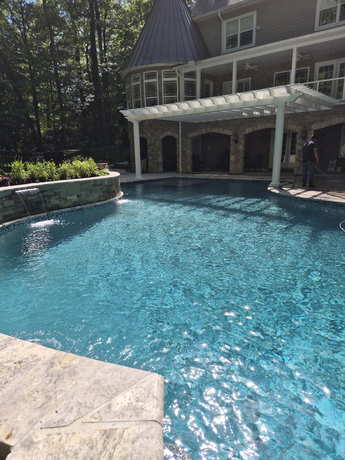 Custom freeform pool with sparkling blue water, stone waterfall and white pergola