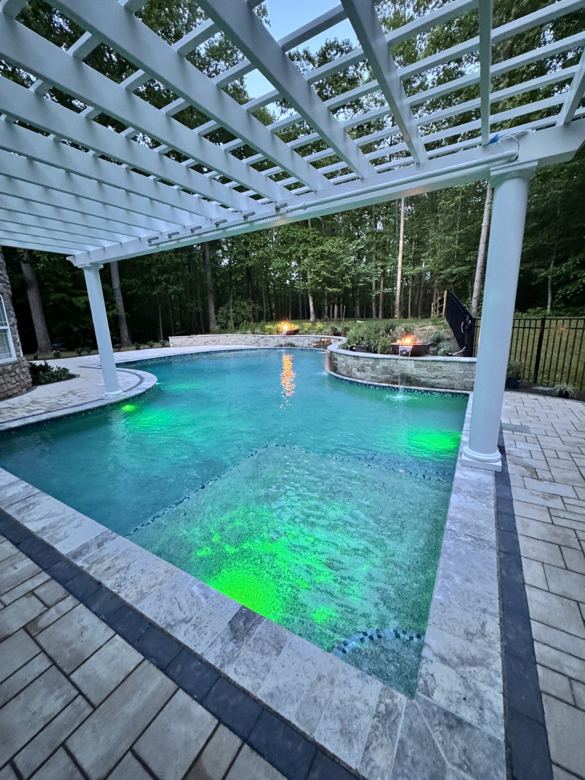 Custom illuminated pool with stone waterfalls and white pergola